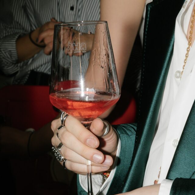 Eine Person in grünem Jackett hält einen roséfarbenen Wein in der Hand