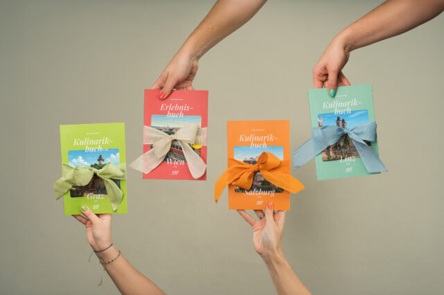 Vier Hände halten die 1000things Bücher – Erlebnisbuch Wien und Kulinarikbücher Graz, Salzburg und Linz – jeweils mit farbigen Geschenk-Schleifen.