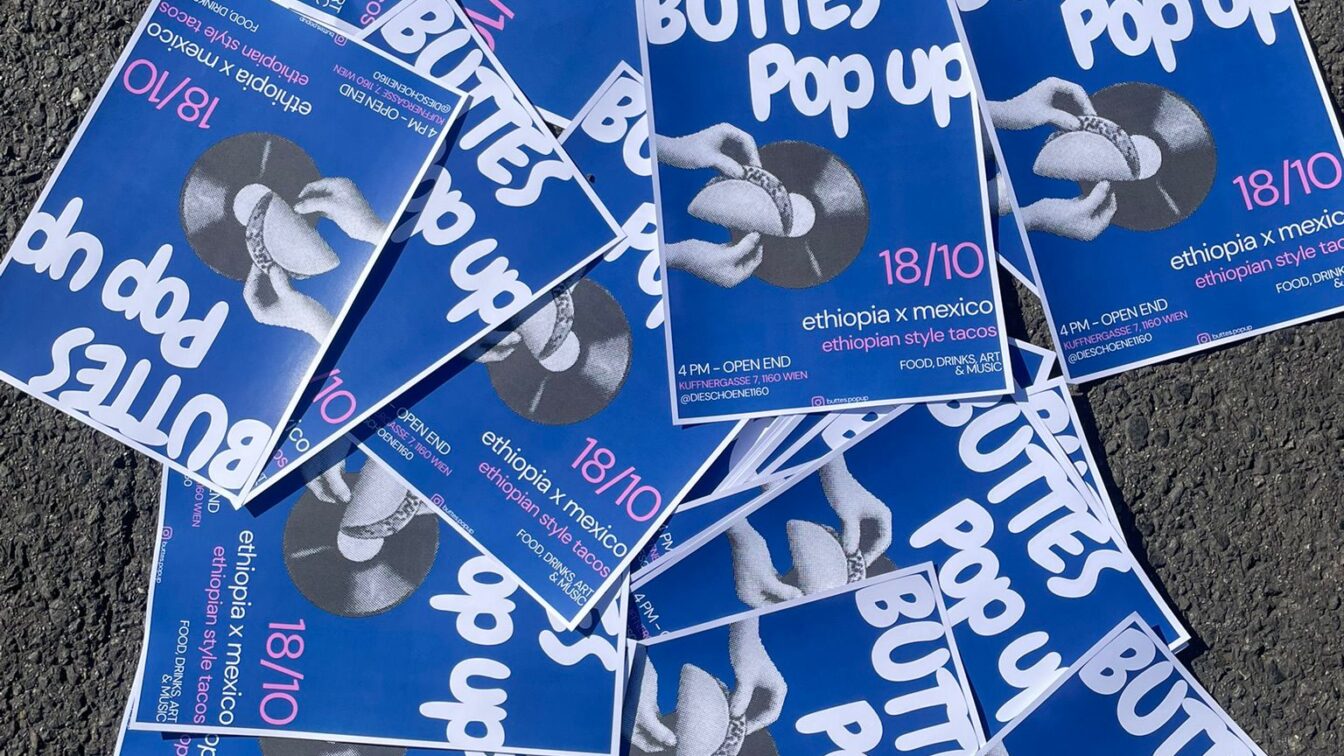 Mehrere blaue Plakate liegen auf Asphalt verteilt. Auf den Plakaten steht in weißer Schrift ‚BUTTES Pop up‘ mit dem Datum 18/10. Darunter steht ‚ethiopia x mexico – ethiopian style tacos‘ sowie weitere Veranstaltungsinformationen. In der Mitte ist ein Schwarz-Weiß-Foto von zwei Händen, die einen Taco halten