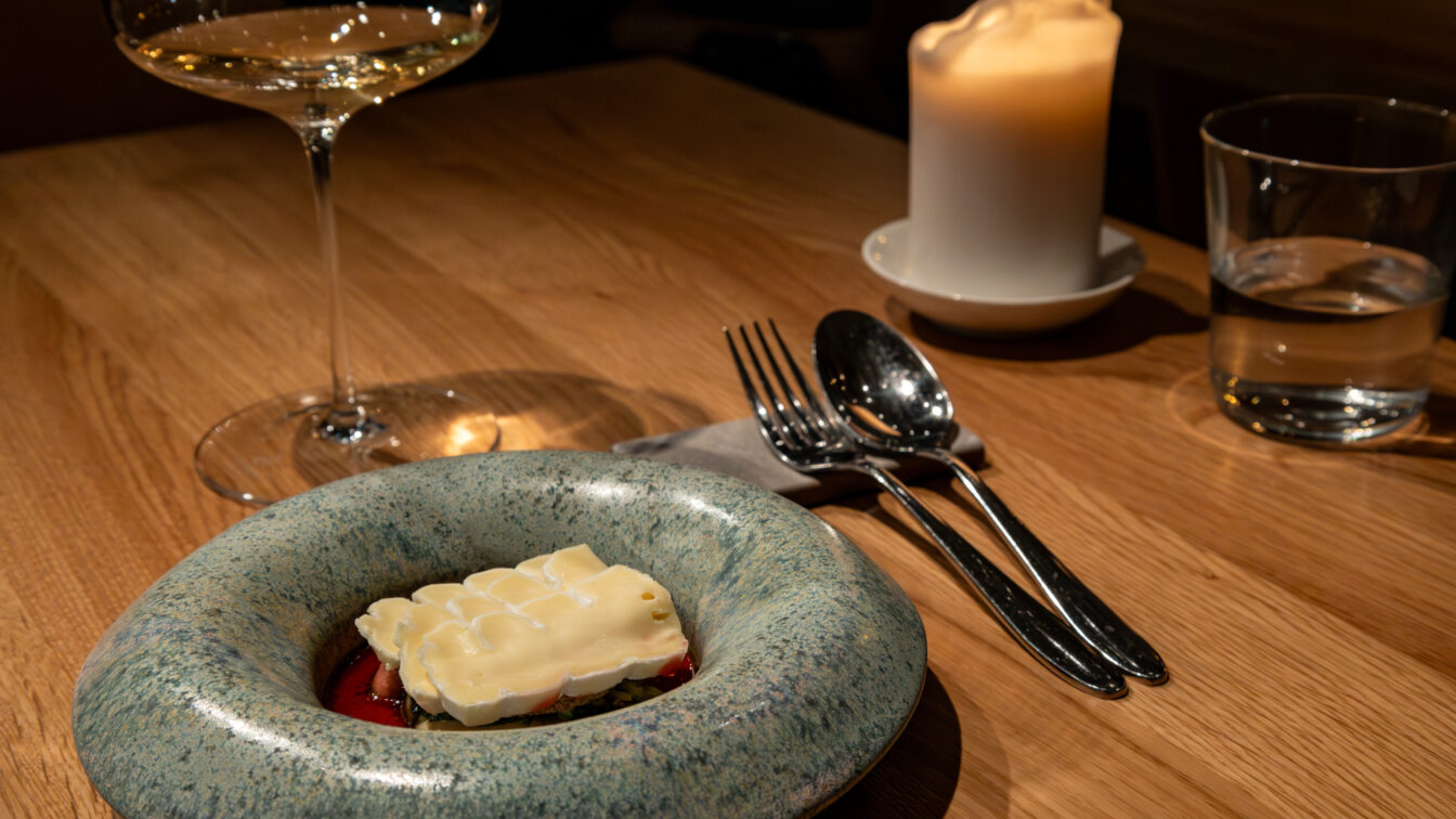 Elegantes Restaurantambiente mit modern angerichtetem Gourmetgericht, Weinglas, Besteck und Kerze auf einem Holztisch in Berlin.