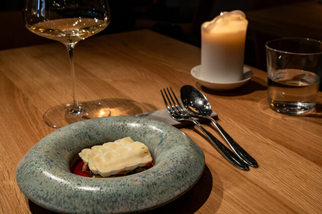 Elegantes Restaurantambiente mit modern angerichtetem Gourmetgericht, Weinglas, Besteck und Kerze auf einem Holztisch in Berlin.