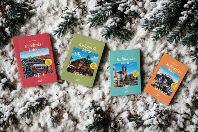 Vier 1000things Bücher – das Erlebnisbuch Wien sowie die Kulinarikbücher Graz, Linz und Salzburg – liegen auf schneebedeckten Tannenzweigen im winterlichen Setting.