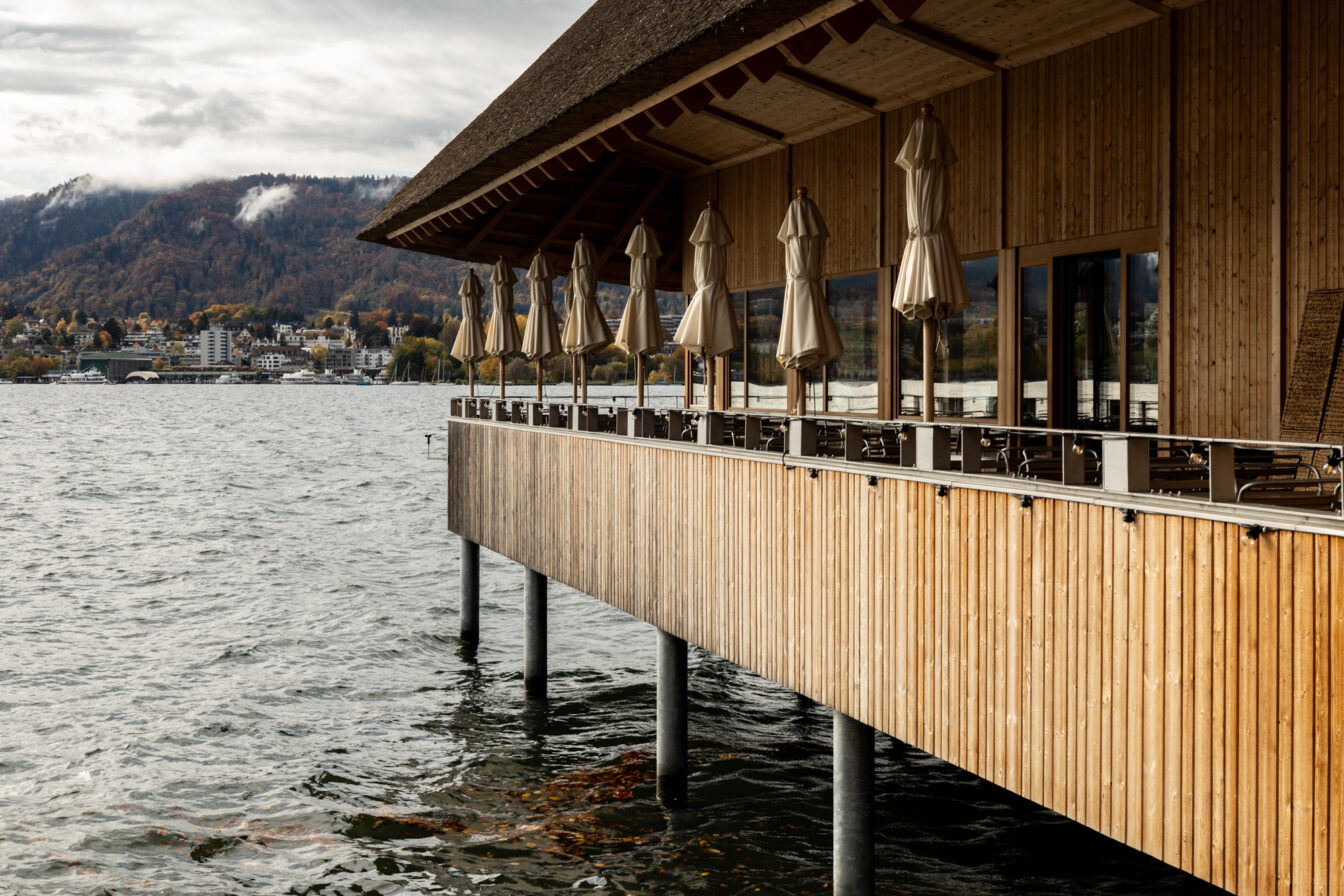 Holzterrasse des Restaurants Fischerstube direkt am Zürichsee mit Sicht auf die umliegenden Berge – ein außergewöhnliches Restaurant in Zürich mit einzigartiger Seelage.