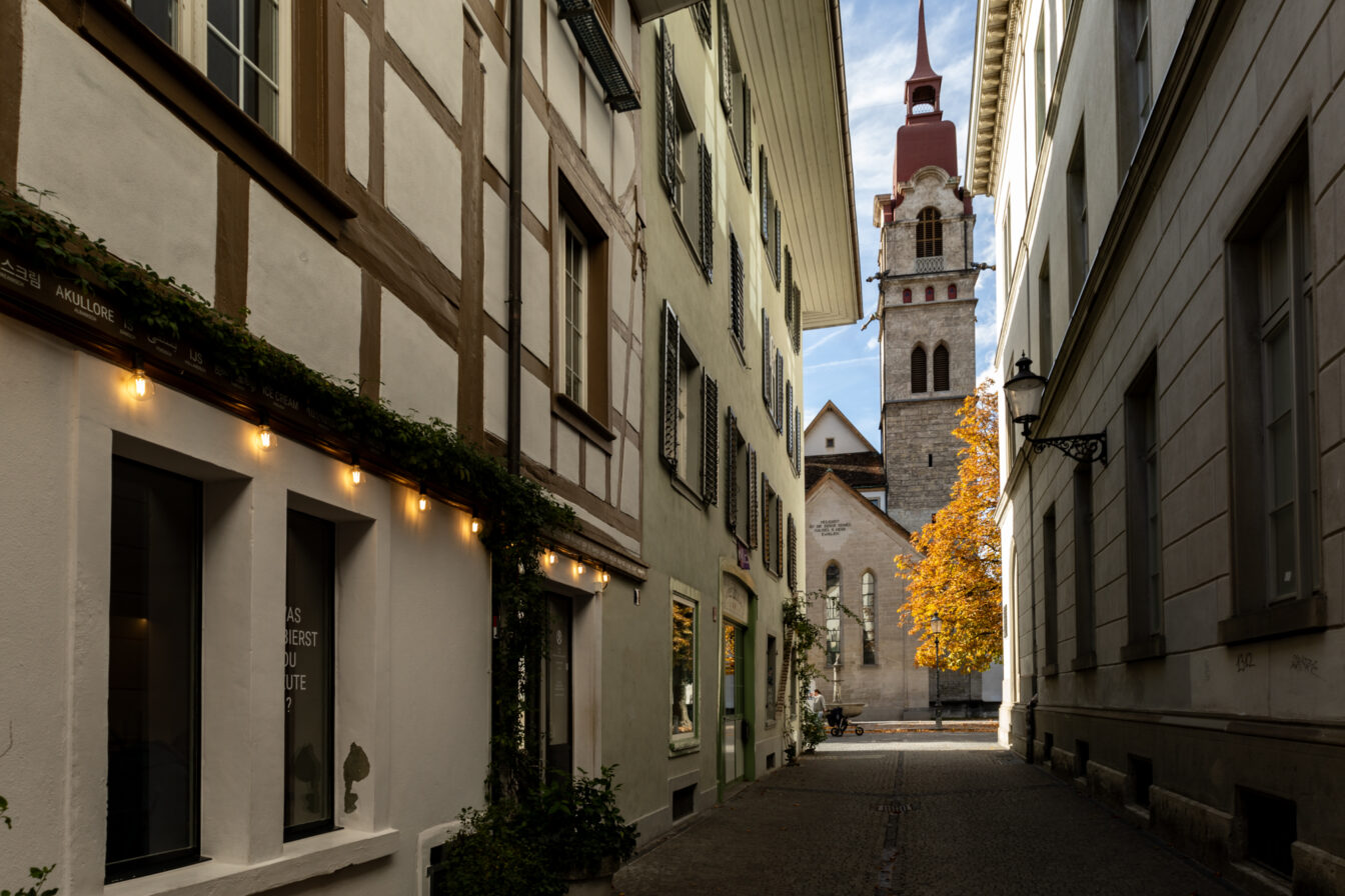 Schmale Gasse in der Altstadt von Winterthur mit Blick auf den Kirchturm und herbstlich gefärbte Bäume – ein malerisches Highlight der Stadt.