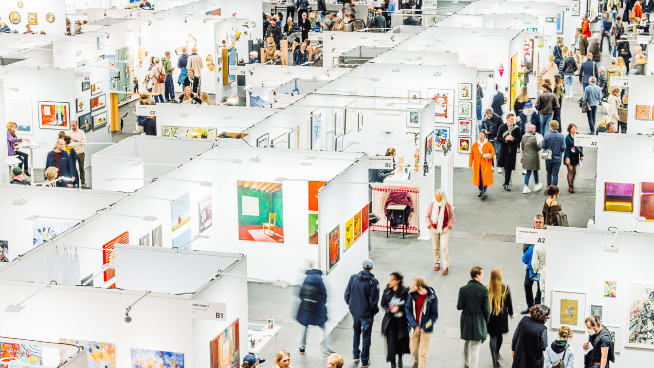 Affordable Art Fair in Wien: Eine Kunstmesse mit weißen Ausstellungsständen, bunten Kunstwerken und vielen Besuchern.