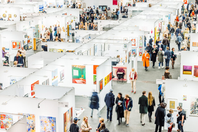 Affordable Art Fair in Wien: Eine Kunstmesse mit weißen Ausstellungsständen, bunten Kunstwerken und vielen Besuchern.