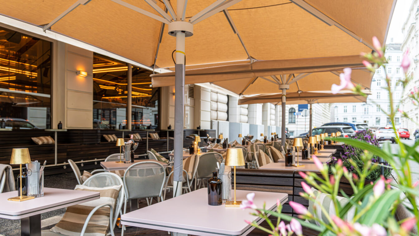 gedeckte Tische stehen unterm Sonnenschirm im Gastgarten der Bar Kleinod am Ring im 1. Bezirk in Wien