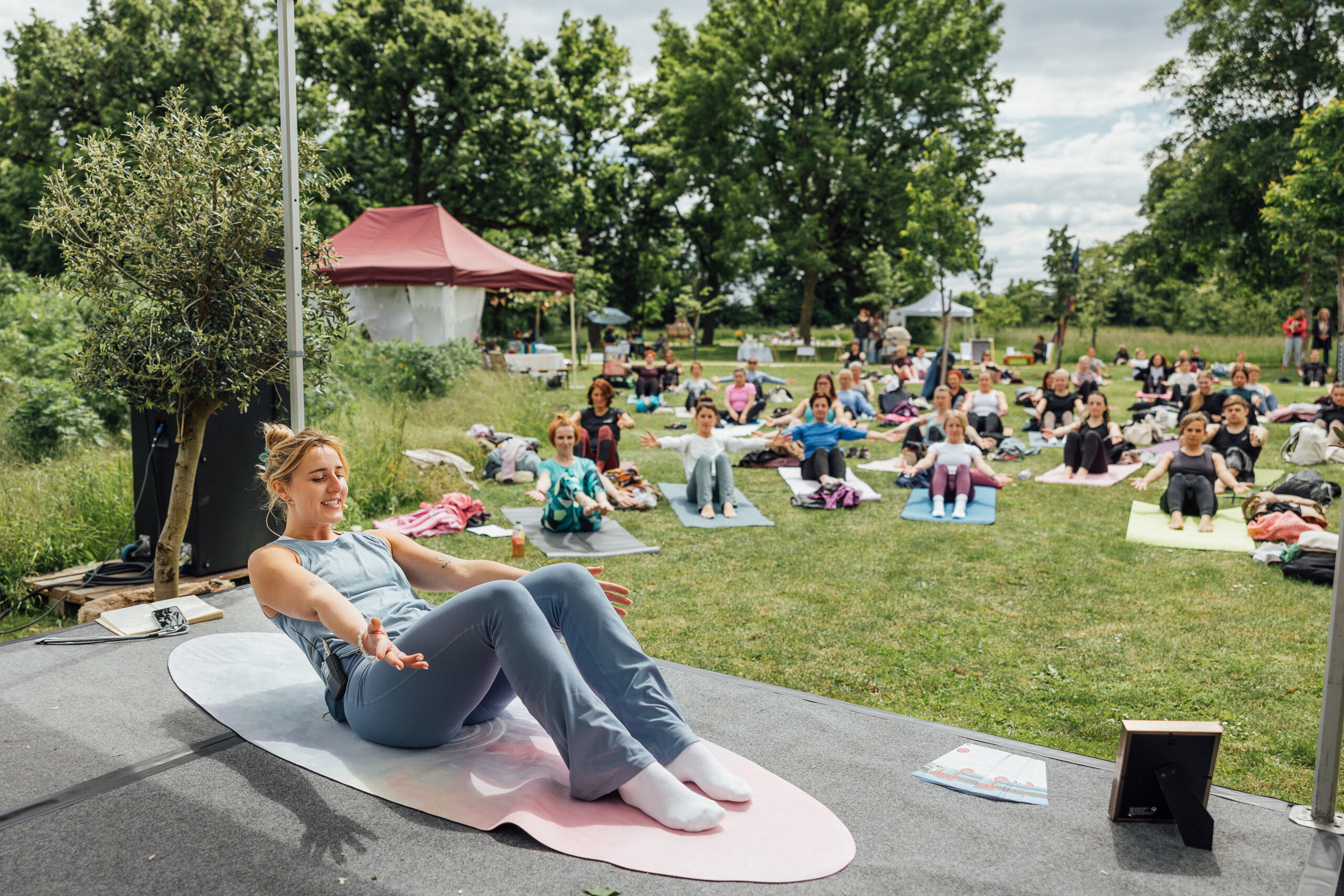 Gemeinsames Yoga im Freien mit einer Lehrerin auf einer Bühne beim Glow & Flow Festival Wiener Neustadt.