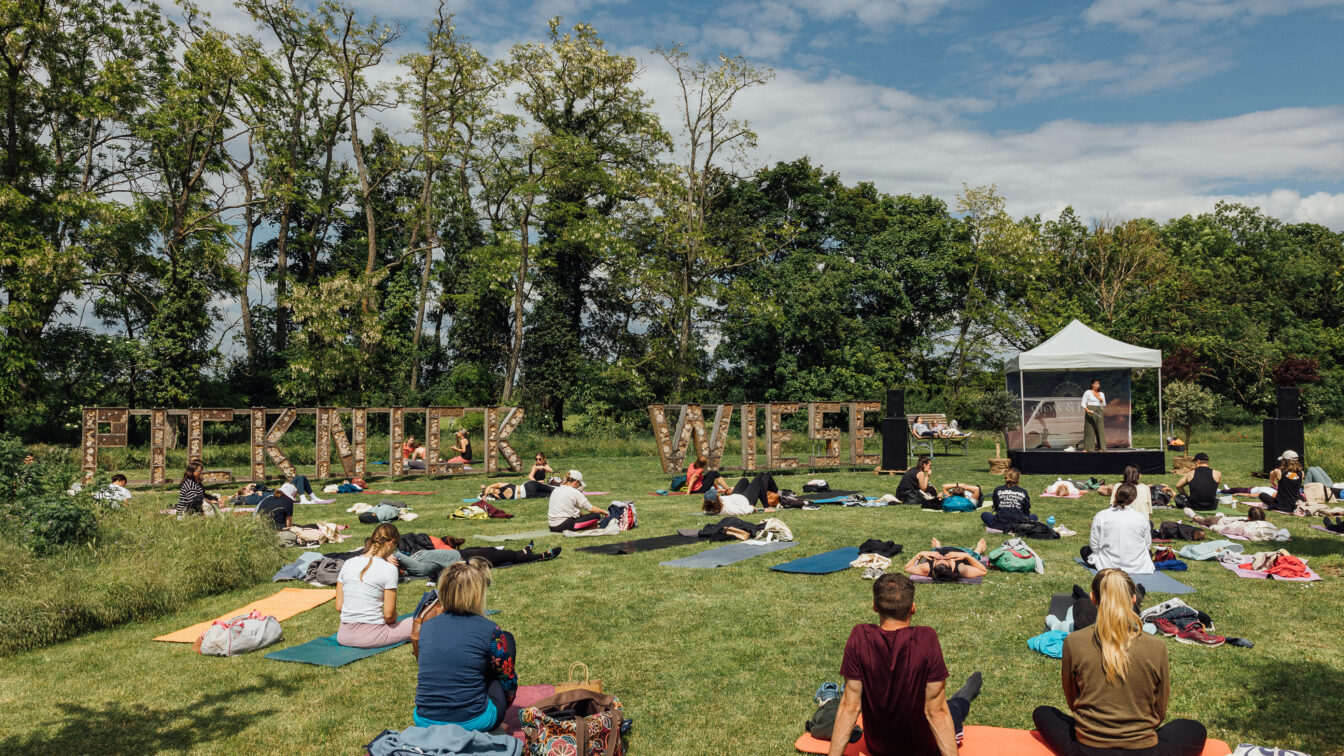 Mehrere Personen sitzen beim Glow & Flow Festival Wiener Neustadt auf einer Yogamatte in der Wiese im Sommer.
