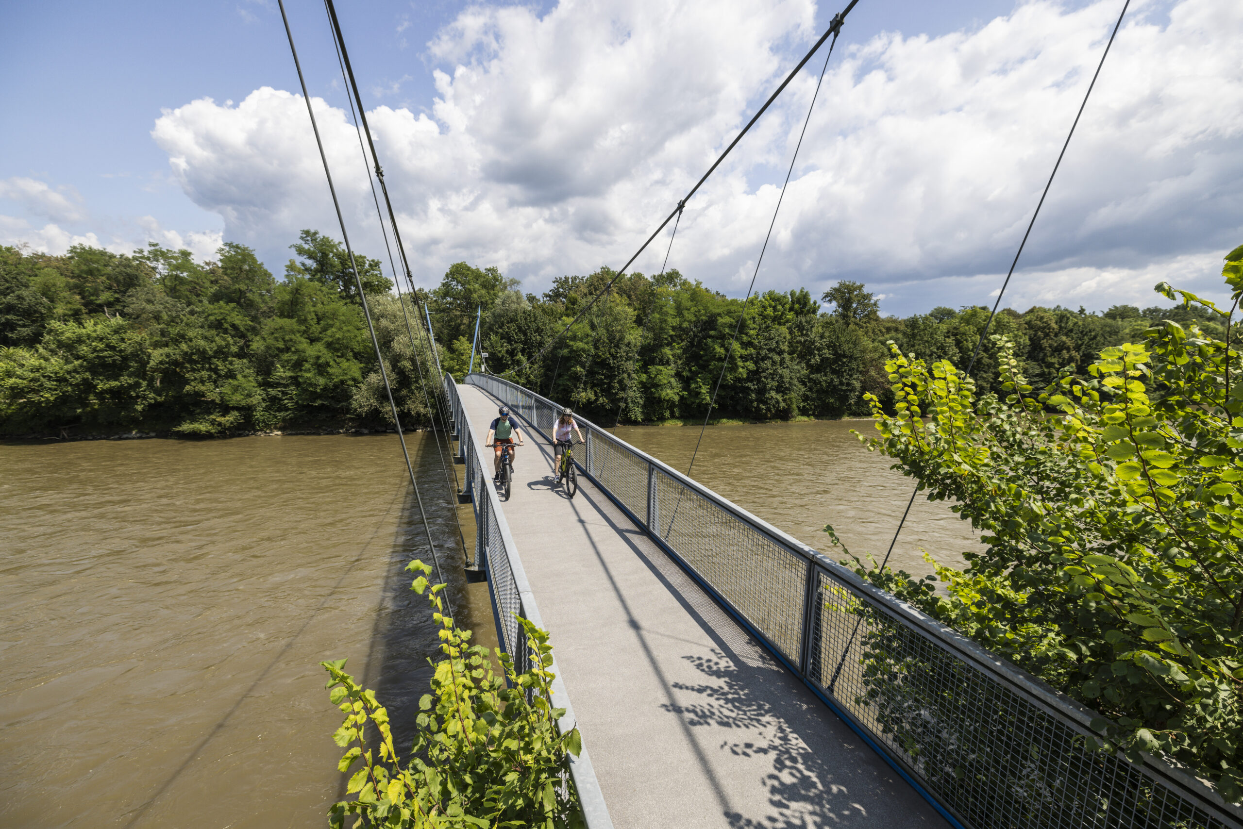 Zwei Radfahrer auf einer Hängebrücke über einem Fluss