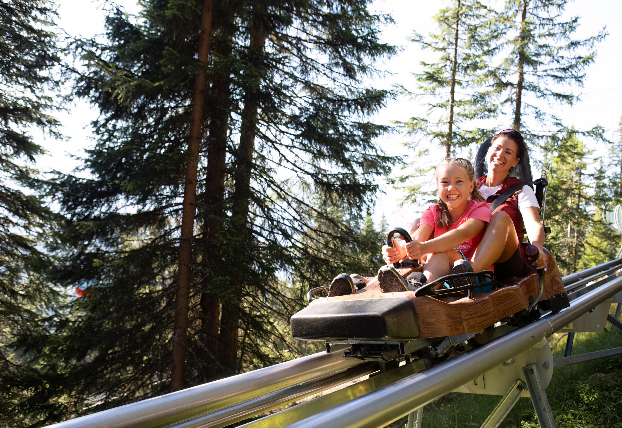 Eine Frau und ein Kind sitzen auf einer Sommerrodel und fahren durch den Wald