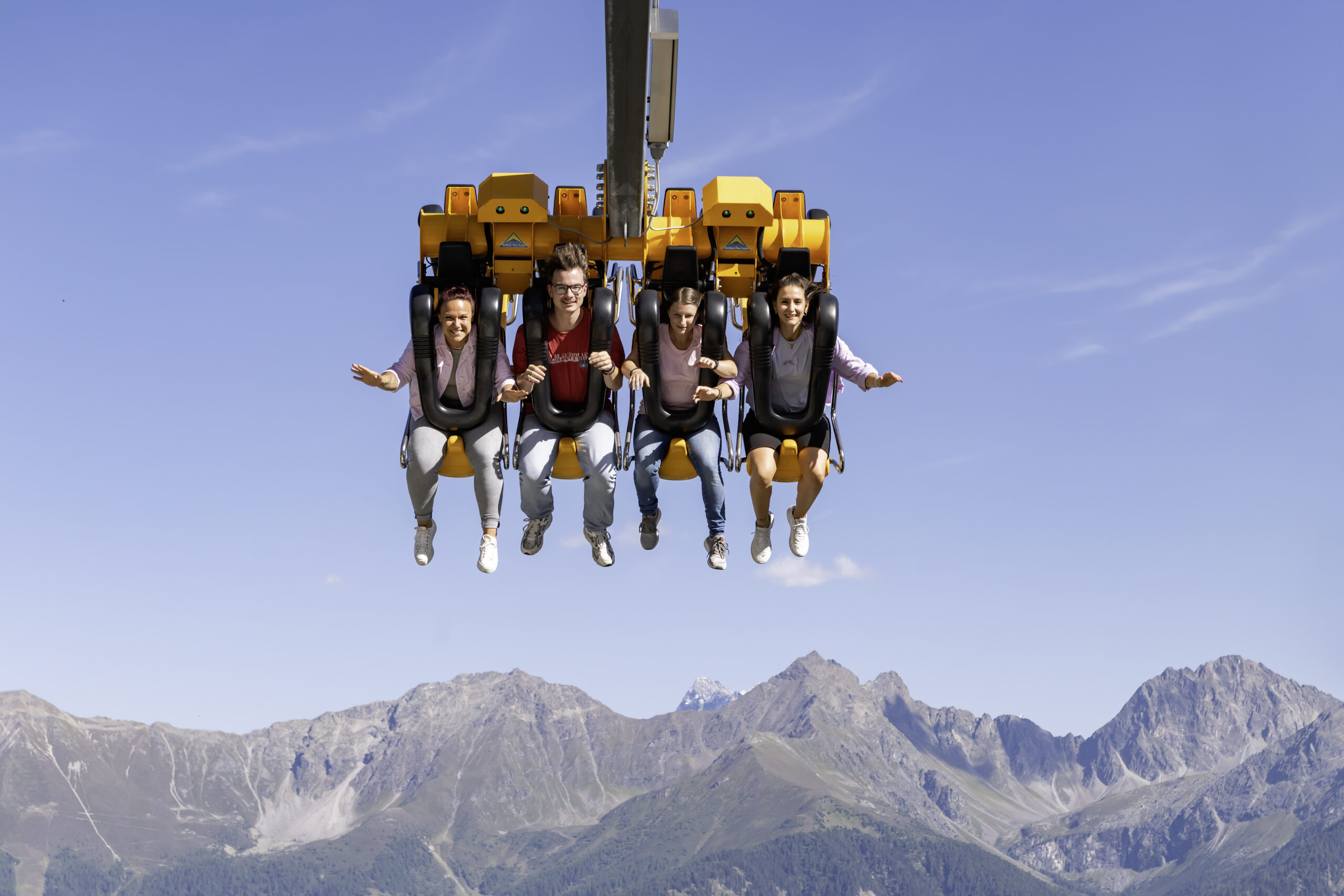 Vier Personen schwingen auf einer Luftschaukel mit Blick aufs Bergpanorama