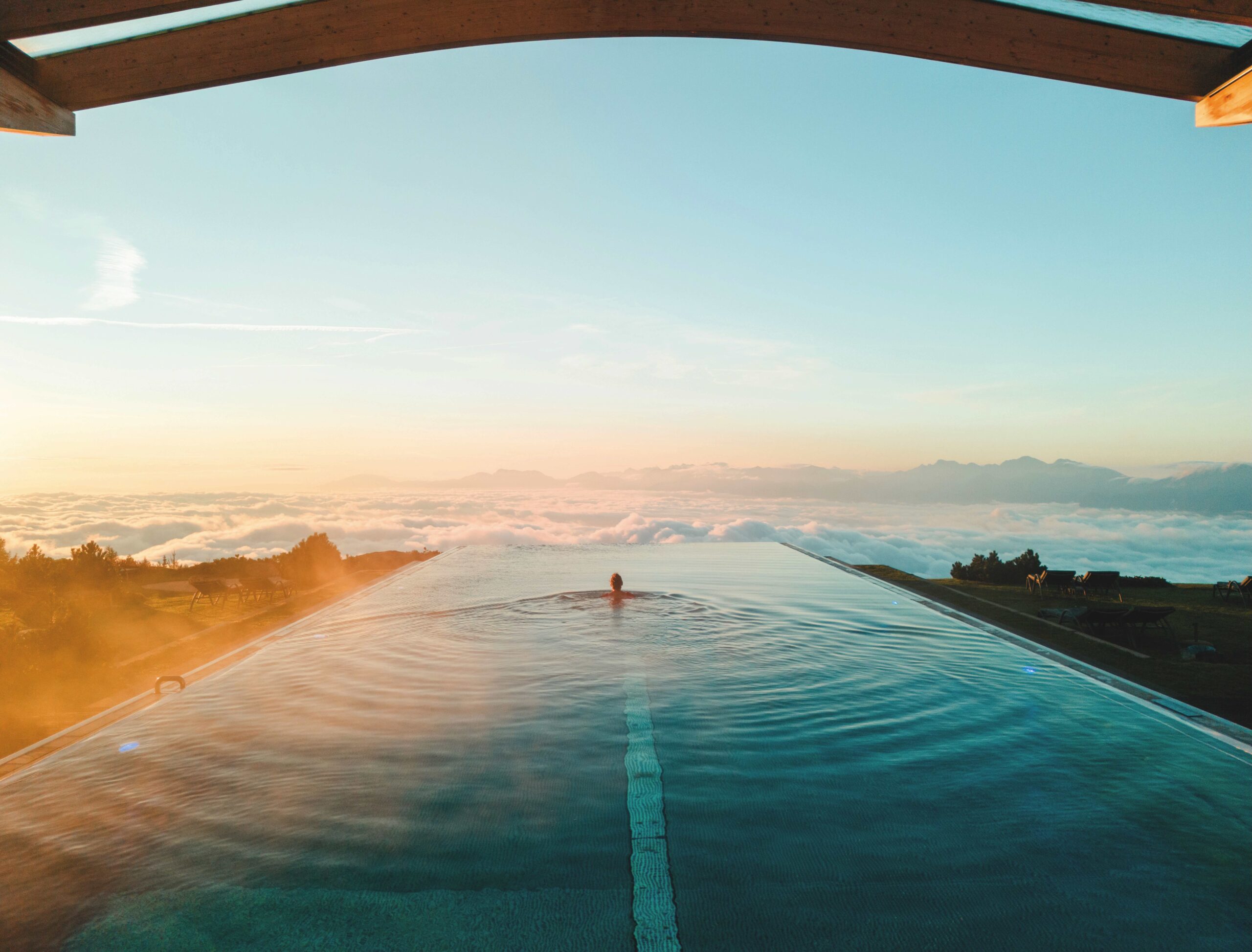Person schwimmt im Unendlichpool am Mountain Resort Feuerberg auf den Rand zu, dahinter sieht man nur Wolken und Bergspitzen.