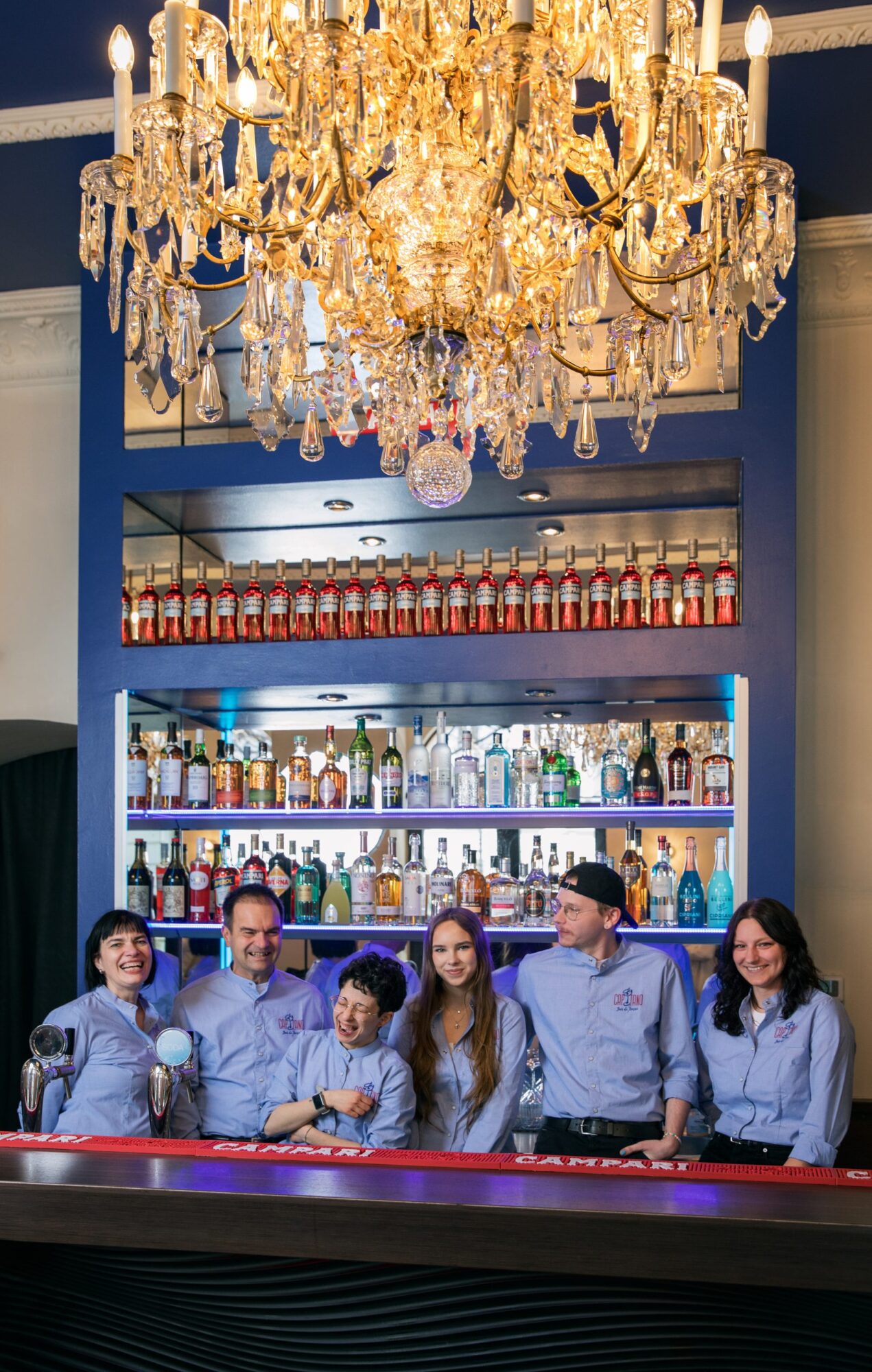 das Team der Aperitivo-Bar Capitano Rossi in Wien steht hinter dem Thresen und unter einem großen Luster