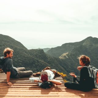 Personen sitzen auf Aussichtspunkt über grüner Berglandschaft