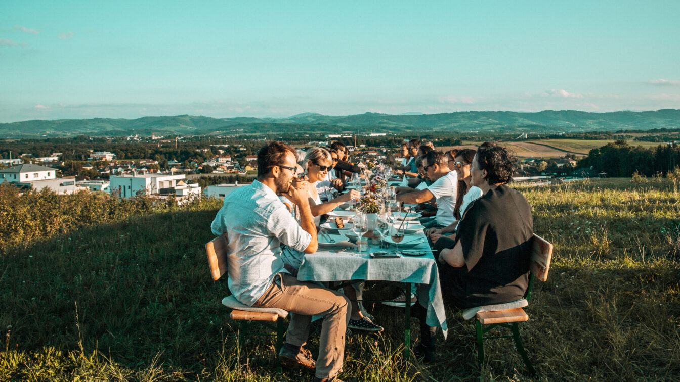 mehrere Menschen sitzen auf einem gedeckten Tisch in der Sonne bei einem Event der Mostviertler Feldversuche