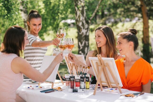 vier Frauen trinken Rosé im Garten und malen eigene Kunstwerke