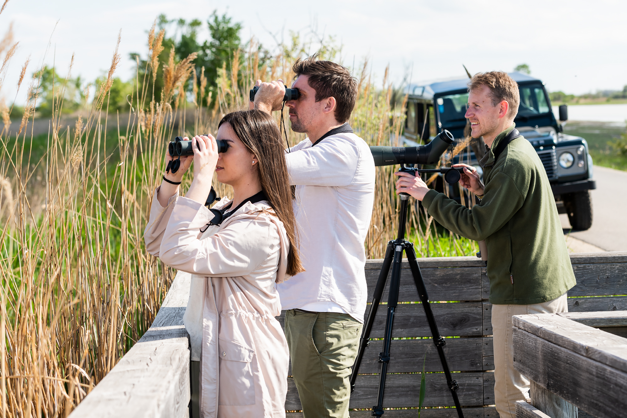 Drei Personen machen eine Safari durch den burgenländischen Seewinkel und beobachten etwas durch Ferngläser.