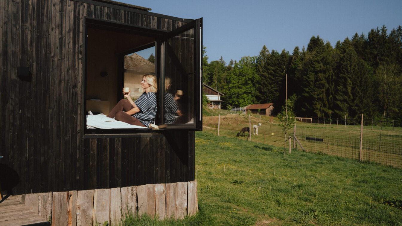 Frau trinkt Kaffee im Fenster einer Cabin und schaut in die Sonne
