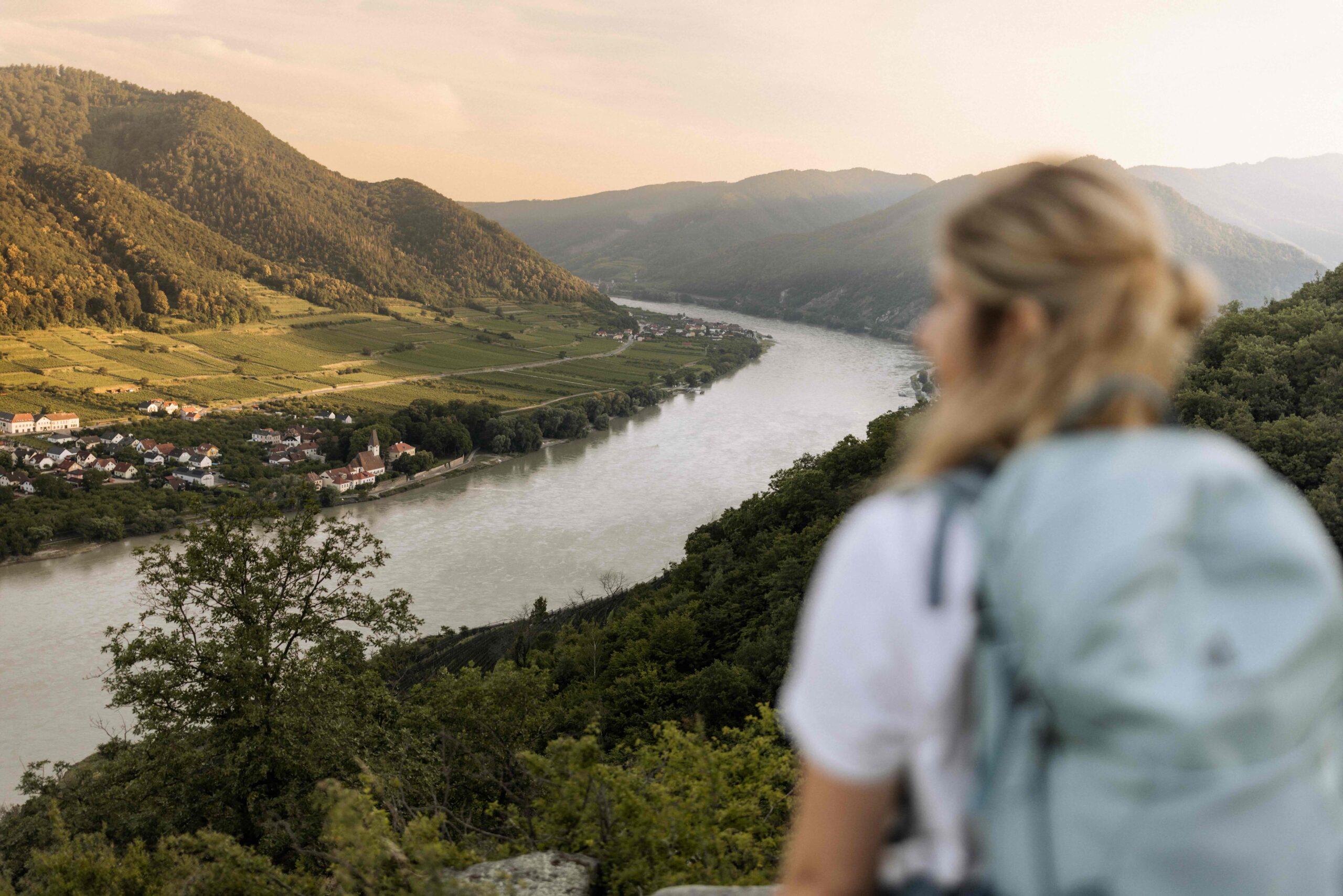 Eine Frau mit Rucksack am Welterbesteig Wachau blickt auf die Donau