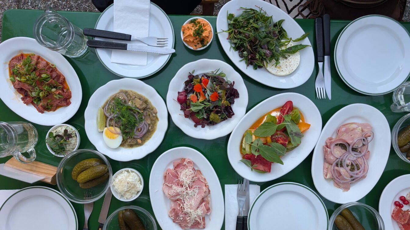 ein gefüllter Tisch mit verschiedenen Heurigen-Speisen im Gastgarten der Buschenschank in Residence in Wien Grinzing