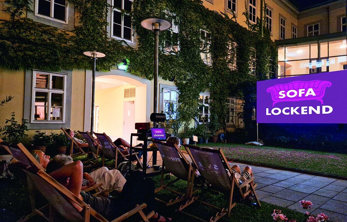 Open Air in Wien: Eine Leinwand im Innenhof des Möbelmuseums, davor Liegestühle mit Zuschauer*innen