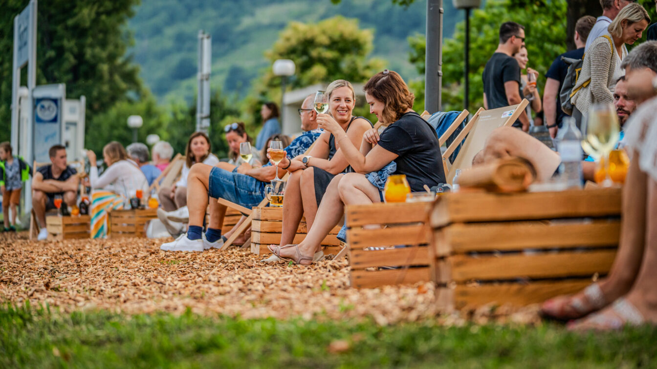 Menschen sitzen auf Liegestühlen und trinken Wein in der Donau Lounge in Spitz an der Donau in Niederösterreich