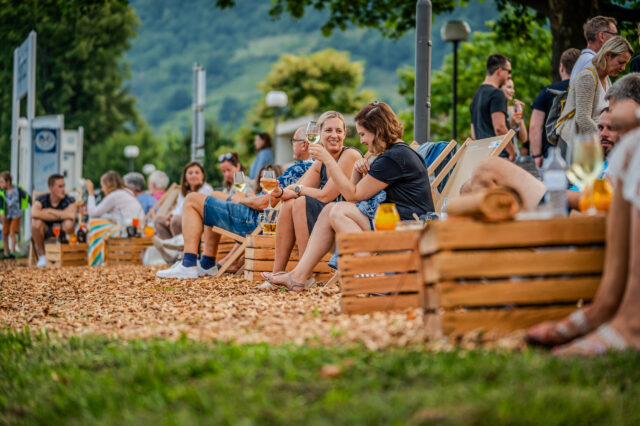 Menschen sitzen auf Liegestühlen und trinken Wein in der Donau Lounge in Spitz an der Donau in Niederösterreich