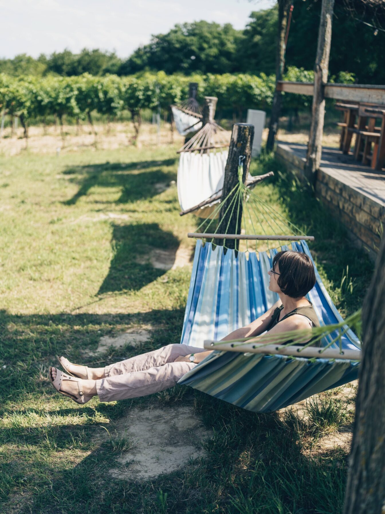 Eine Frau sitzt auf einer Hängematte in einem Weingarten und blickt in die Natur