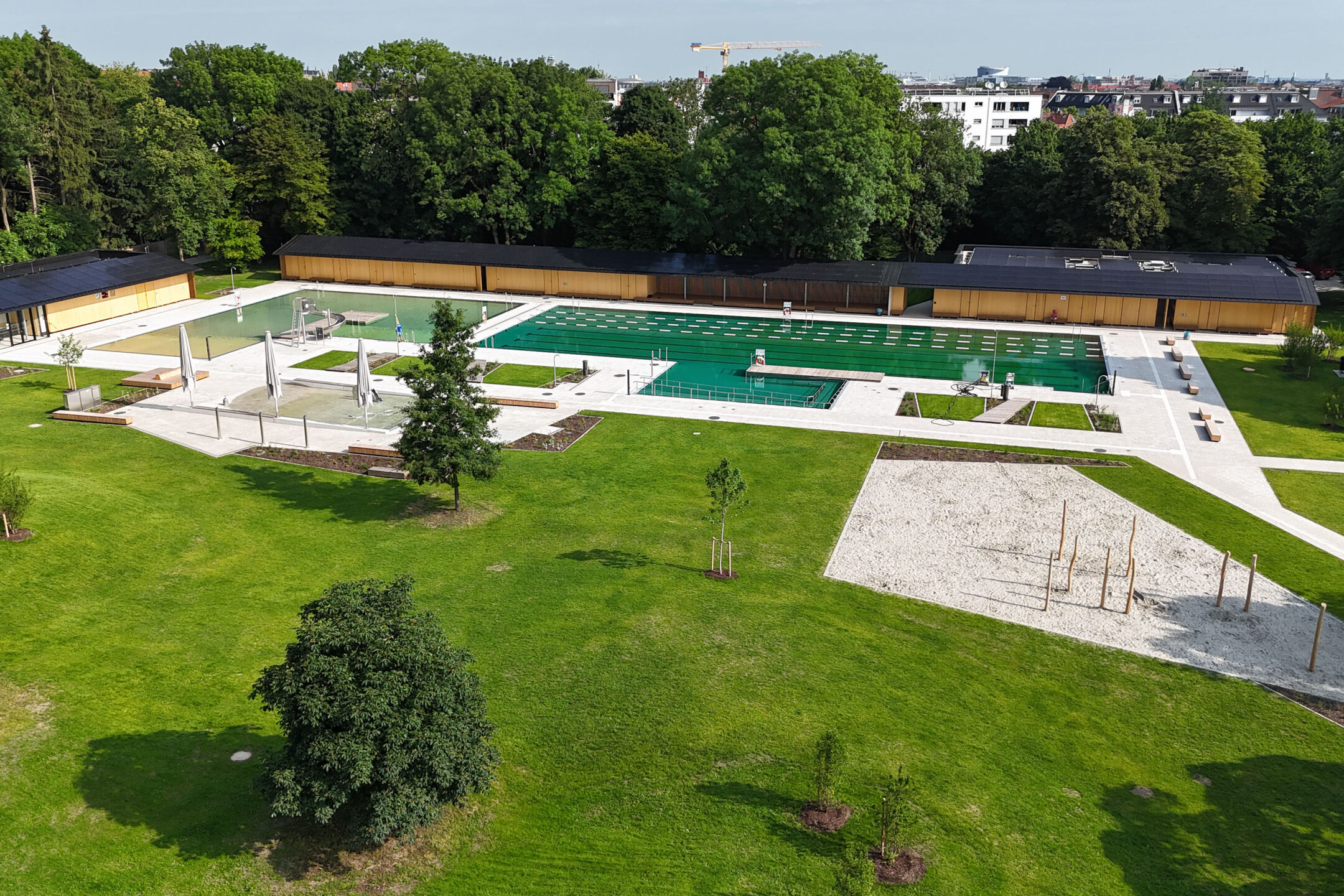 Weitläufige Grünfläche und ein naturbelassener Pool in einem Freibad in München.