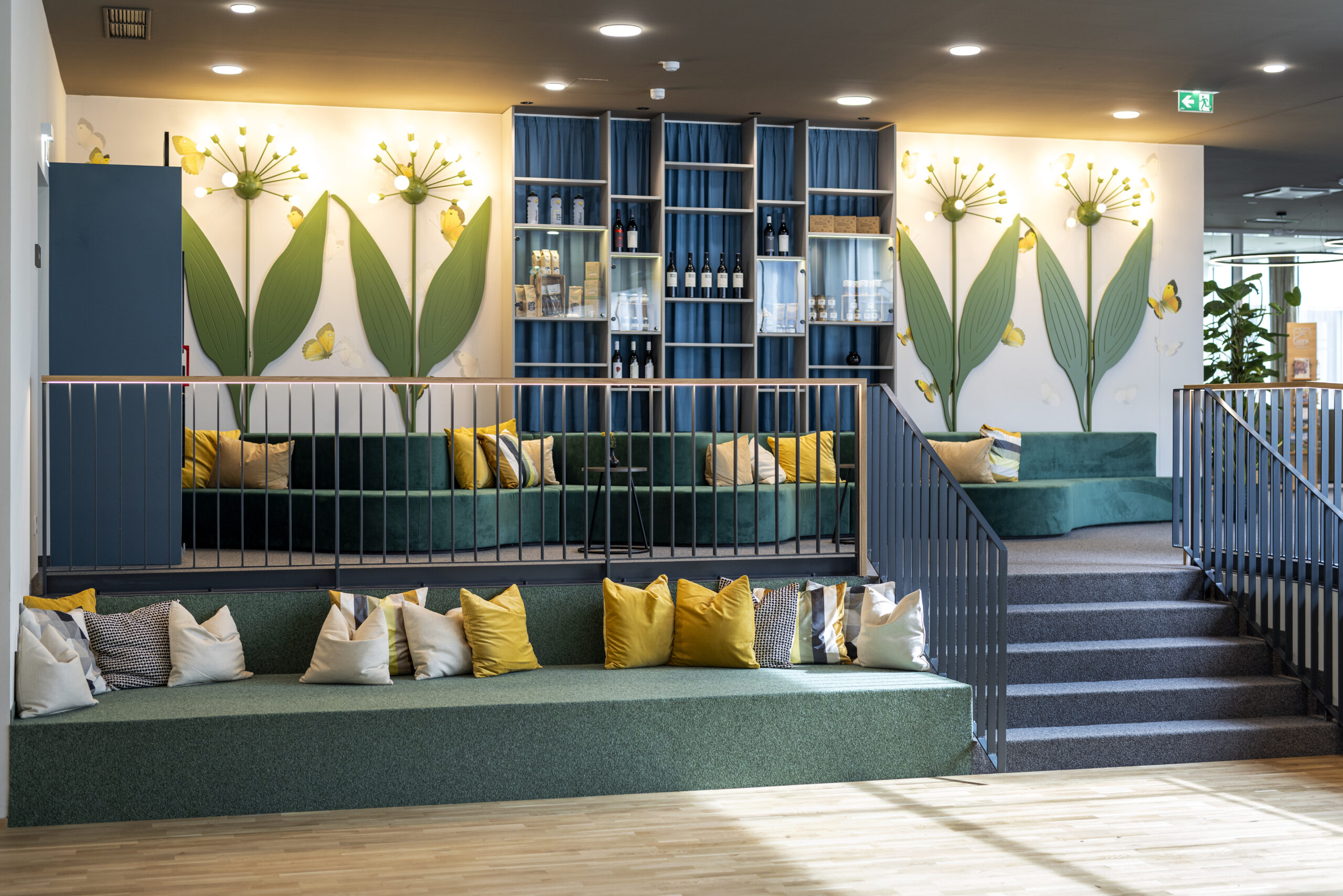 Sie sehen gemütliche Sitmöglichkeiten mit farbigen Pölstern sowie den Regionalshop im Hintergrunnd in der Lobby des JUFA Hotel Bad Radkersburg