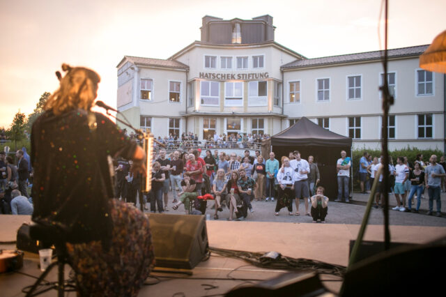 ein Open-Air-Live-Konzert findet am Gelände des OKH Vöcklabruck statt; im Vordergrund die Künstlerin, im Hintergrund das Publikum und das OKH-Gebäude