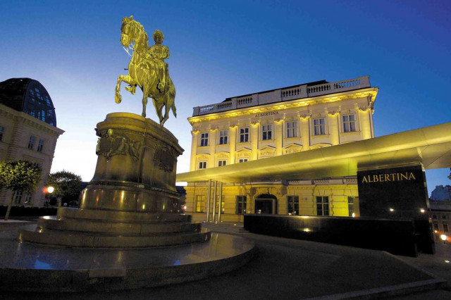 Ein Foto der nächtlich beleuchteten Albertina Wien, im Vordergrund die Statue eines Reiters