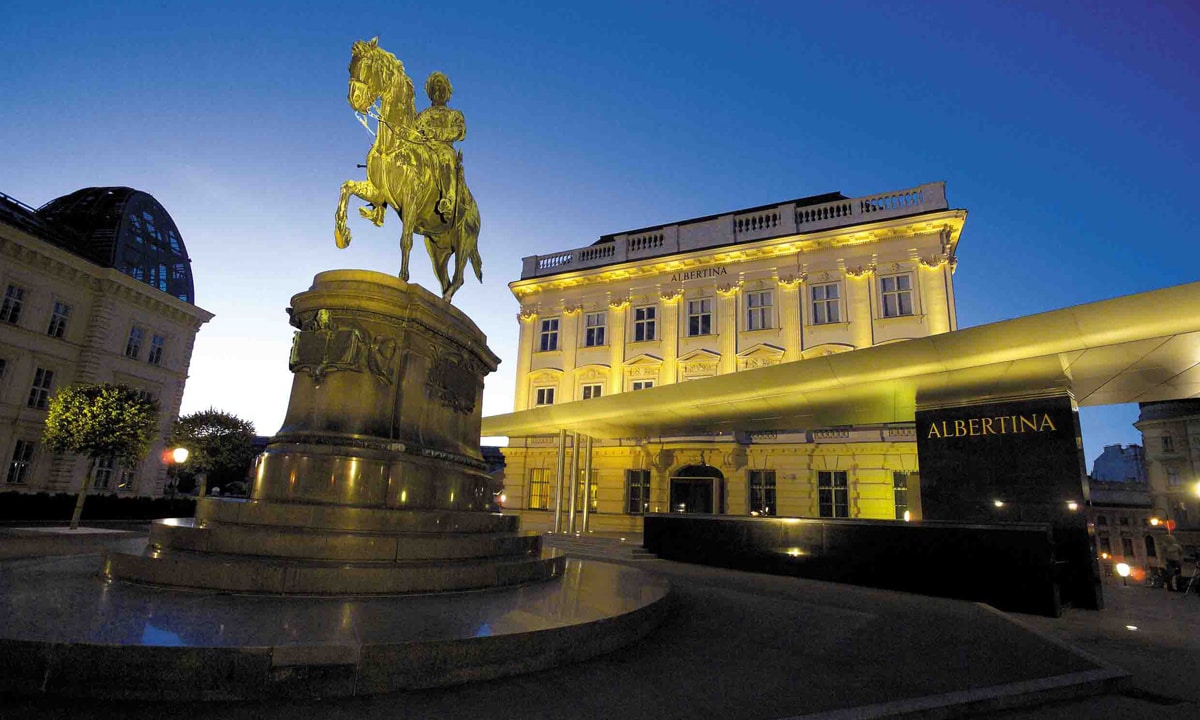Ein Foto der nächtlich beleuchteten Albertina Wien, im Vordergrund die Statue eines Reiters
