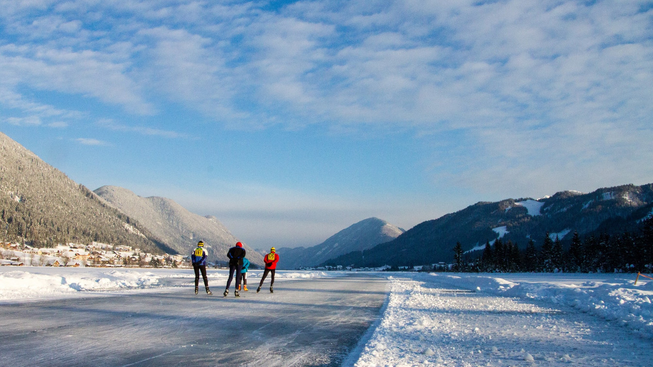 Drei Eisläufer*innen, die am zugefrorenen Weissensee in Kärnten eislaufen.