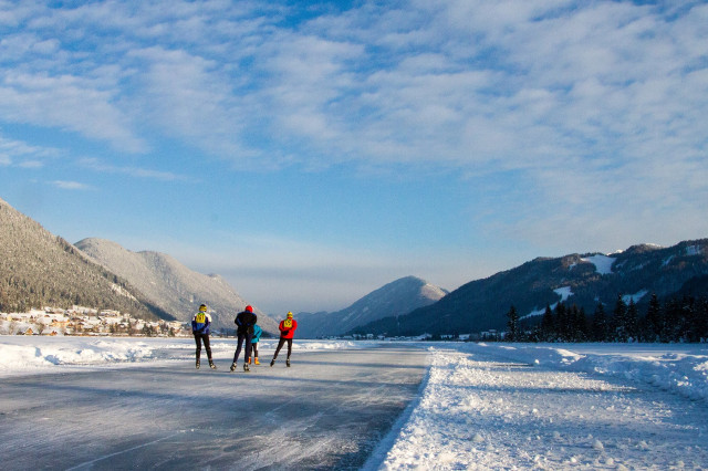 Drei Eisläufer*innen, die am zugefrorenen Weissensee in Kärnten eislaufen.